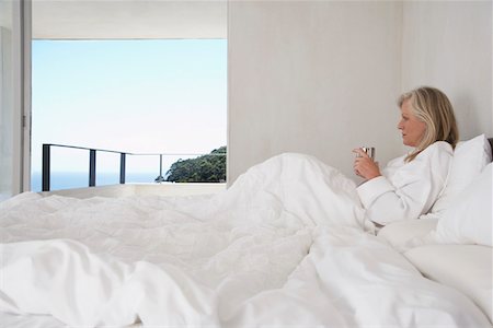simsearch:693-03707745,k - Mature woman in bathrobe, holding cup, lying in bed, side view Stock Photo - Premium Royalty-Free, Code: 693-03707746