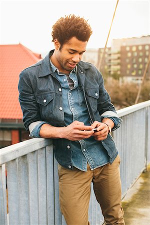 standing on a bridge - Young man texting on an iPhone in an urban setting. Stock Photo - Rights-Managed, Code: 700-06701842
