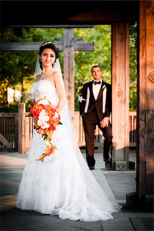 Portrait of bride standing outdoors in public garden, with groom standing in background, Ontario, Canada Stock Photo - Rights-Managed, Code: 700-07199862