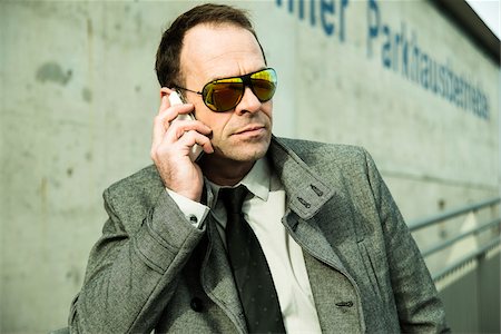 Close-up portrait of businessman wearing sunglasses and overcoat, using cell phone outdoors, Germany Stock Photo - Rights-Managed, Code: 700-07529270