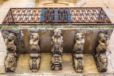 simsearch:700-08723105,k - Low angle view of balcony with carved, stone supports and old, metal railing in Modica in the Province of Ragusa in Sicily, Italy Stock Photo - Rights-Managed, Code: 700-08723126