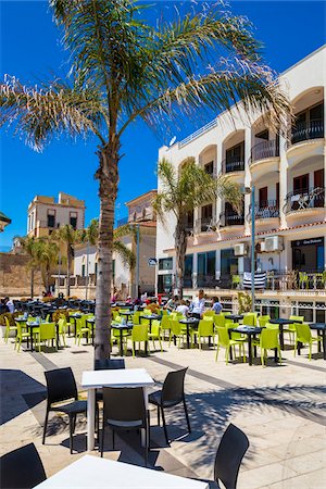 Modern tables and chairs in an open area patio surrounded by historic buildings in Marina di Ragusa in Sicily, Italy Stock Photo - Rights-Managed, Code: 700-08723135