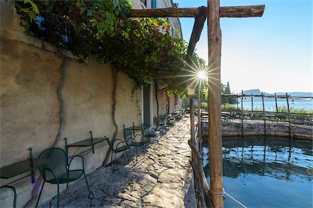 Sun shining on the stone patio at Locanda San Vigilio overlooking a little harbor and Lake Garda in the morning at Punta San Vigilio in Garda, Veneto, Italy Stock Photo - Rights-Managed, Code: 700-09022535