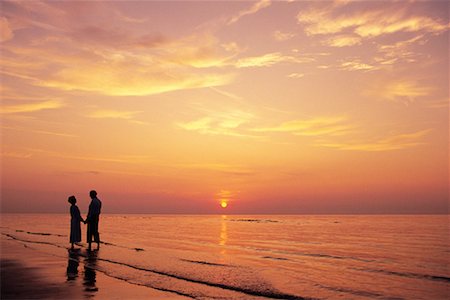 simsearch:700-00021491,k - Mature Couple debout en Surf sur la plage, main dans la main au coucher du soleil Photographie de stock - Rights-Managed, Code: 700-00077507