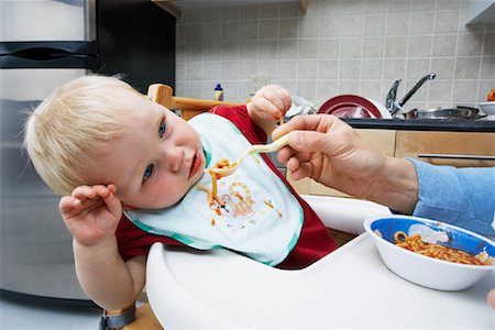 Parent Feeding Spaghetti to Boy in High Chair Foto de stock - Con derechos protegidos, Código: 700-00934490