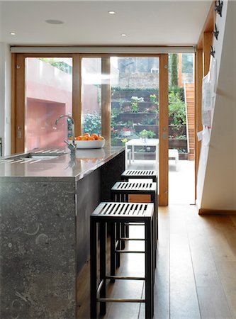 Bar stools at breakfast bar with full-height glass doors to garden, UK. Architects: STUDIO BEDNARSKI LTD Stock Photo - Rights-Managed, Code: 845-05837805