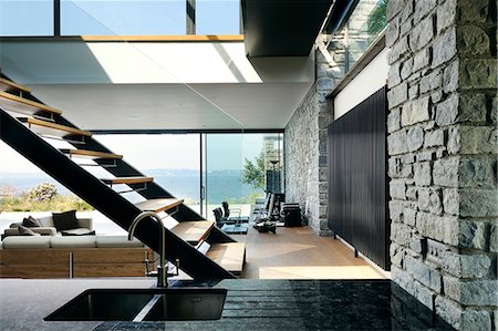 simsearch:700-06038236,k - The interior spaces of a modern house on the cliffs overlooking the sea. Large glass panels and walls, and wooden shelves and room dividers.  Floating staircase. Stock Photo - Rights-Managed, Code: 845-08939618
