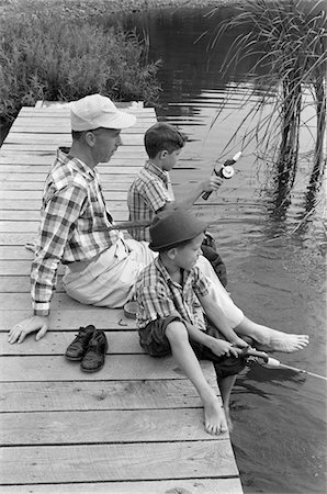 1950s - 1960s FATHER WITH TWO SONS SITTING ON DOCK FISHING TOGETHER OUTDOOR BY POND Stock Photo - Rights-Managed, Code: 846-05645856