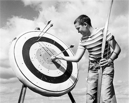 release - 1960s BOY JEANS STRIPED T-SHIRT HOLDING BOW & PULLING ARROW OUT OF TARGET BULL'S-EYE Stock Photo - Rights-Managed, Code: 846-05645870