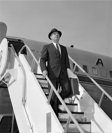 simsearch:846-05645846,k - 1960s BUSINESSMAN DEPLANING FROM AIRPLANE WEARING HAT AND CARRYING OVERCOAT AND BRIEFCASE Foto de stock - Con derechos protegidos, Código: 846-05645897