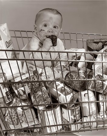 1960s BABY SITTING IN SUPERMARKET CART FULL OF CANS EATING CANDY BAR WITH A MESSY FACE Foto de stock - Con derechos protegidos, Código: 846-05646041