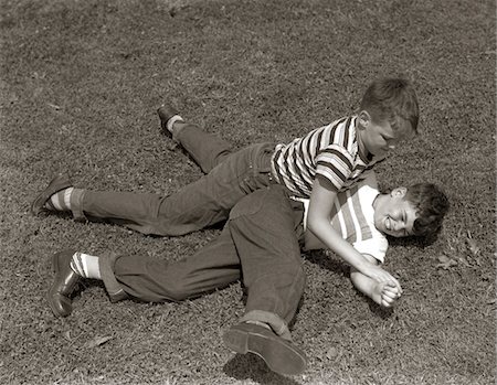 play fights - 1950s TWO BOYS WEAR TEE SHIRTS BLUE JEANS PLAYING ROUGH FIGHTING WRESTLING ON THE GRASS Stock Photo - Rights-Managed, Code: 846-05646112