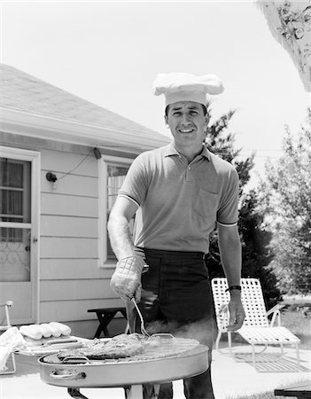 ANNÉES 1960 SOURIANT HOMME OUTDOORS IN BACKYARD TOQUE PORTE PATIO CUISSON DES STEAKS HOT-DOGS SUR GRILL Photographie de stock - Rights-Managed, Code: 846-05646234