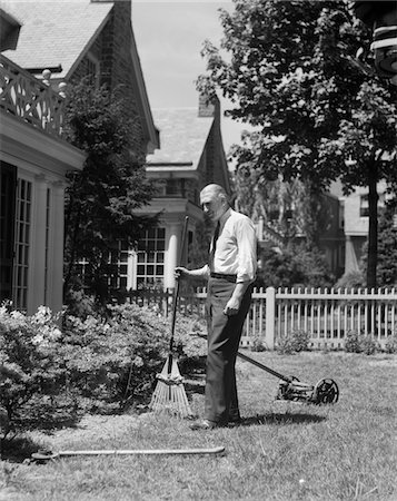 1930s SENIOR MAN STANDING BY GARDEN SHRUBS WITH RAKE PUSH MOWER LAWNMOWER BEHIND HIM Stock Photo - Rights-Managed, Code: 846-05646384