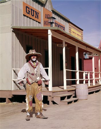 1960s SAD CLOWN IN COWBOY COSTUME STANDING IN STREET OF WESTERN FRONTIER TOWN Stock Photo - Rights-Managed, Code: 846-05646742