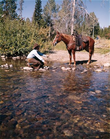 simsearch:846-05645665,k - 1970s COWBOY IN STREAM KNEELING TRY TO LEAD HORSE INTO WATER Stock Photo - Rights-Managed, Code: 846-05647018