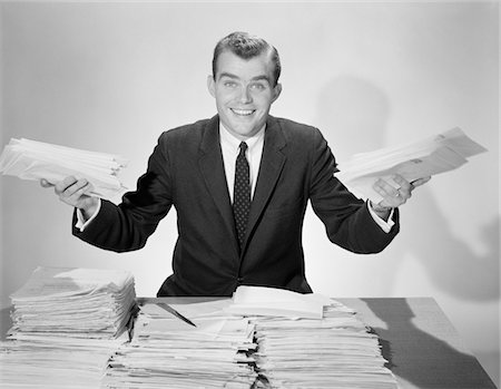 simsearch:846-02795767,k - 1950s AMUSED SMILING BUSINESSMAN HOLDING PAPERS FROM THE PILES ON HIS DESK Stock Photo - Rights-Managed, Code: 846-05647734