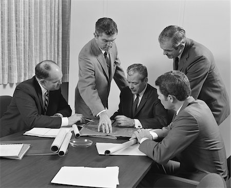 simsearch:846-05648290,k - 1960s 5 EXECUTIVE BUSINESSMEN AT CONFERENCE TABLE MEETING LOOKING OVER PAPERS & BLUEPRINTS Stock Photo - Rights-Managed, Code: 846-05647763