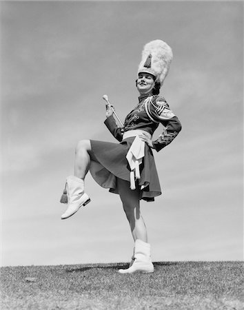 simsearch:846-05647924,k - 1950s SMILING MAJORETTE POSING OUTDOORS WEARING UNIFORM WITH SHORT SKIRT BOOTS TALL FURRY HAT HOLDING A BATON Stock Photo - Rights-Managed, Code: 846-05647920