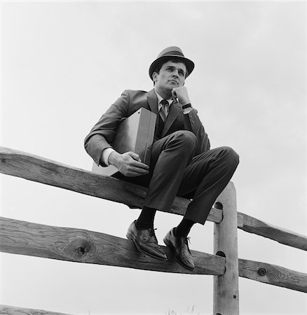 simsearch:846-08639518,k - 1970s BUSINESSMAN SITTING ON FENCE WORRIED EXPRESSION HOLDING BRIEFCASE Stock Photo - Rights-Managed, Code: 846-05648248