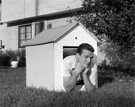 simsearch:846-08140107,k - 1960s MAN IN DOGHOUSE IN BACKYARD RESTING ON ELBOWS WITH FROWN ON FACE Stock Photo - Rights-Managed, Code: 846-05648374