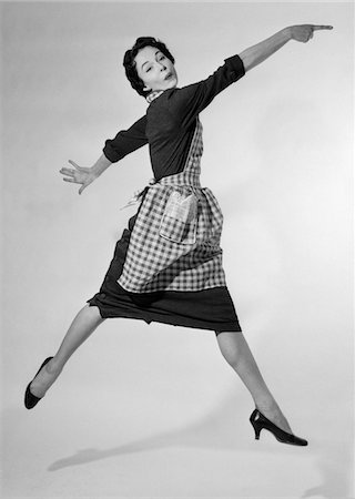 simsearch:846-06111898,k - 1950s WOMAN HOUSEWIFE IN GINGHAM APRON RUNNING AND JUMPING INTO AIR SMILING AND POINTING INDEX FINGER STUDIO HIGH HEEL SHOES Stock Photo - Rights-Managed, Code: 846-05648370
