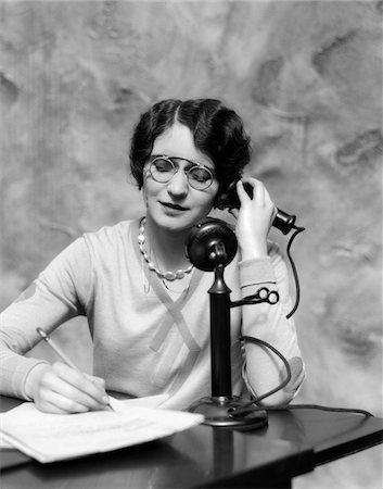 simsearch:846-02796457,k - 1920s WOMAN WEARING PINCE-NEZ GLASSES SITTING AT DESK TALKING ON CANDLESTICK PHONE AND WRITING Stock Photo - Rights-Managed, Code: 846-05648449