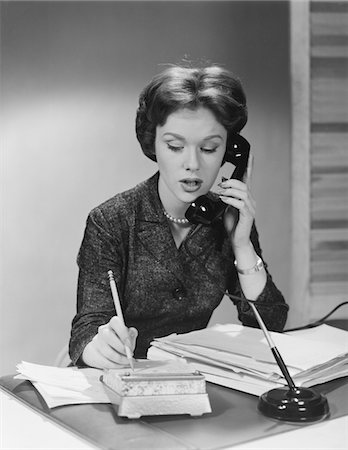 simsearch:846-02796457,k - 1950s - 1960s BRUNETTE BUSINESS WOMAN SITTING DESK TALKING TELEPHONE WRITING NOTE ON CALENDAR Stock Photo - Rights-Managed, Code: 846-05648455