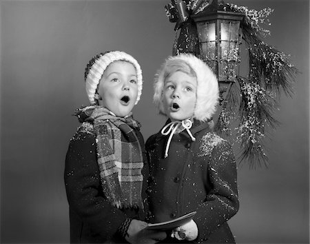 simsearch:846-05648541,k - 1960s BOY AND GIRL SINGING CHRISTMAS CAROL TOGETHER UNDER SNOWY OUTDOOR PORCH LIGHT Stock Photo - Rights-Managed, Code: 846-05648543