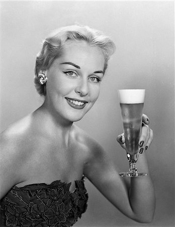 simsearch:846-05646926,k - 1950s WOMAN WEARING STRAPLESS EVENING GOWN HOLDING UP TALL PILSNER GLASS OF BEER LOOKING AT CAMERA Stock Photo - Rights-Managed, Code: 846-06111786