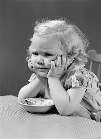 simsearch:846-03165636,k - 1940s GIRL AT TABLE WITH HEAD CRADLED IN BOTH HANDS FROWN ON HER FACE A CEREAL BOWL AND SPOON BETWEEN HER ELBOWS ON TABLE Stock Photo - Rights-Managed, Code: 846-06111812