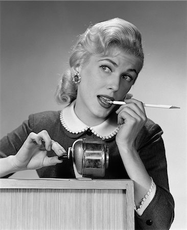 1950s DISTRACTED BLOND WOMAN OFFICE WORKER AT PENCIL SHARPENER LOOKING OFF TO SIDE WITH PENCIL IN MOUTH Stock Photo - Rights-Managed, Code: 846-06111838