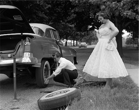 simsearch:846-06112141,k - 1950s TEENAGE BOY CROUCHING DOWN CHANGING FLAT TIRE PROM DATE WATCHING WITH HANDS ON HIPS Stock Photo - Rights-Managed, Code: 846-06112157