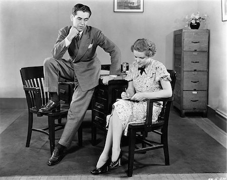 1940s BUSINESSMAN LEANING AGAINST DESK WITH FOOT PROPPED ON CHAIR LEERING OGLING SECRETARY SITTING NEXT TO HIM TAKING NOTES Stock Photo - Rights-Managed, Code: 846-06112226