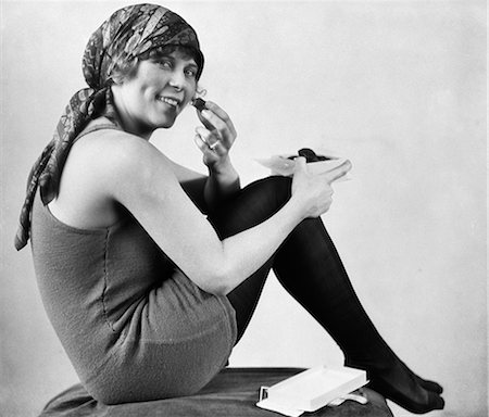 1920s WOMAN IN OLD FASHIONED BATHING SUIT WITH SCARF ON HEAD SEATED WITH KNEES TO CHEST EATING CHOCOLATES LOOKING AT CAMERA Stock Photo - Rights-Managed, Code: 846-06112253
