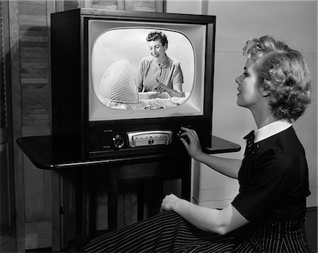 1950s BLONDE WOMAN TURNING DIAL ON TV SET WATCHING PROGRAM ABOUT BABY CHILDCARE Stock Photo - Rights-Managed, Code: 846-06112361