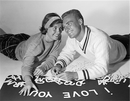 simsearch:846-07200088,k - 1960s SMILING COLLEGIATE COUPLE LYING ON STOMACHS WITH HEADS PRESSED TOGETHER SPELLING OUT I LOVE YOU WITH CUT-OUT LETTERS Stock Photo - Rights-Managed, Code: 846-06112417