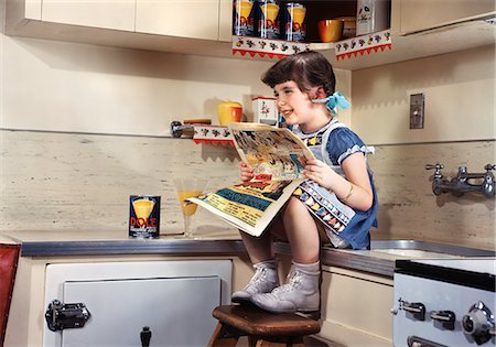 suburban kitchen - 1950s SMILING GIRL SITTING ON KITCHEN COUNTER READING SUNDAY COMICS FUNNIES Photographie de stock - Rights-Managed, Code: 846-07200102