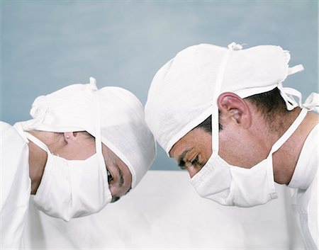 simsearch:846-05647696,k - 1960s COUPLE MAN WOMAN DOCTOR & NURSE WHITE SURGICAL CAP & MASK HEAD TO HEAD IN PROFILE OPERATIONG LOOKING DOWN Stock Photo - Rights-Managed, Code: 846-07760723