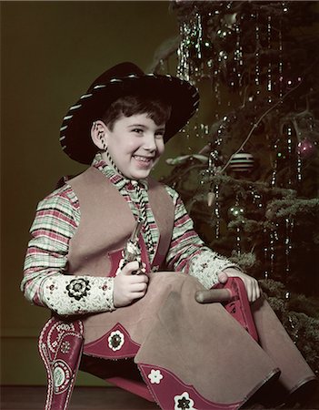 1950s SMIILING BOY COWBOY HAT COSTUME HOLDING TOY GUN BY CHRISTMAS TREE Photographie de stock - Rights-Managed, Code: 846-08030404