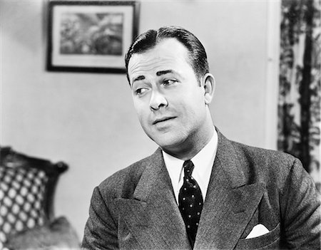 1950s PORTRAIT OF MAN INSIDE LIVING ROOM WEARING SUIT AND TIE LOOKING OFF TO ONE SIDE THINKING CONTEMPLATIVE FUNNY EXPRESSION Stock Photo - Rights-Managed, Code: 846-08140096