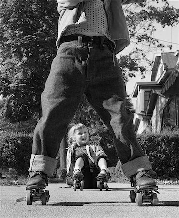 1950s GIRL FALLEN SITTING SIDEWALK WEAR METAL ROLLER SKATES SHOT THROUGH LEGS OF BOY ROLLED CUFF BLUE JEANS Stock Photo - Rights-Managed, Code: 846-08226114