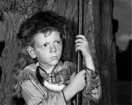 1950s BOY WEARING RACCOON SKIN HAT FRINGED WESTERN STYLE JACKET WITH POWDER HORN AND ANTIQUE RIFLE Stock Photo - Rights-Managed, Code: 846-08226120