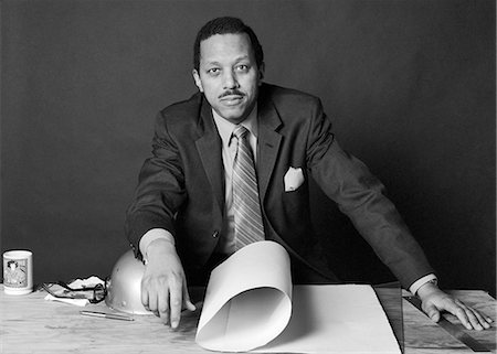simsearch:846-05648291,k - 1970s AFRICAN-AMERICAN BUSINESSMAN CONTRACTOR ARCHITECT BUILDER AT TABLE WITH BUILDING PLANS AND HARD HAT LOOKING AT CAMERA Stock Photo - Rights-Managed, Code: 846-08512748