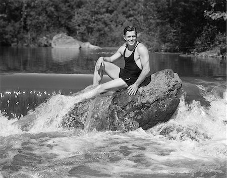 simsearch:846-05648202,k - 1930s SMILING MAN LOOKING AT CAMERA WEARING BATHING SUIT TANK TOP SWIM TRUNKS POSING SITTING ON LARGE ROCK IN WOODLAND POND Stock Photo - Rights-Managed, Code: 846-08639576