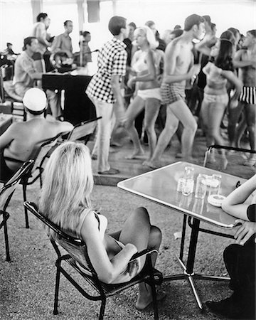 1960s LONG BLONDE HAIR WOMAN SITTING WATCHING GROUP OF YOUNG SPRING BREAK TEENS DANCING WEARING BEACH BATHING SUITS SEASIDE Foto de stock - Con derechos protegidos, Código: 846-09012727