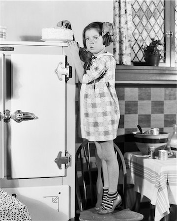 suburban kitchen - 1920s 1930s LITTLE GIRL STANDING ON KITCHEN CHAIR TO REACH CAKE ON TOP OF ICE BOX Photographie de stock - Rights-Managed, Code: 846-09012735