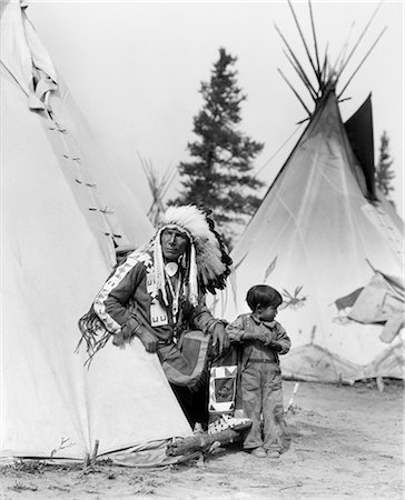 1920s NATIVE AMERICAN INDIAN MAN CHIEF SITTING EAGLE AND BOY IN ENTRANCE TO TEPEE STONEY TRIBE OF BANFF ALBERTA CANADA Stock Photo - Rights-Managed, Code: 846-09012788