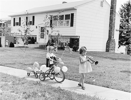 simsearch:846-05647924,k - 1960s GIRL WITH BUGLE LEADING SISTER ON TRICYCLE DECORATED WITH BALLOONS AMERICAN FLAGS FOR JULY 4TH HOLIDAY SIDEWALK PARADE Stock Photo - Rights-Managed, Code: 846-09012794