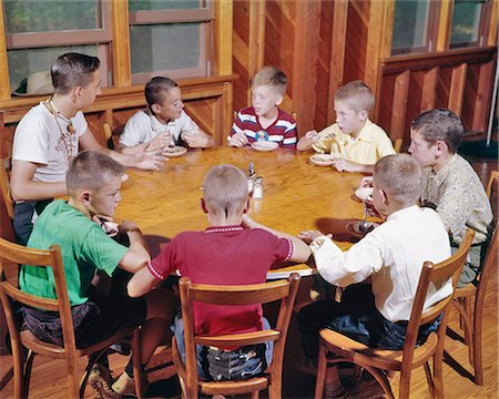 round table - 1960s YOUNG TEENAGE MAN CAMP COUNCILOR SITTING AT WOODEN ROUND TABLE EATING ICE CREAM TALKING WITH SEVEN KIDS BOY CAMPERS Stock Photo - Rights-Managed, Code: 846-09012858